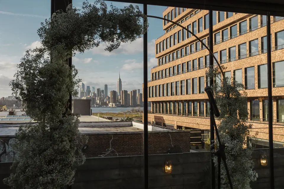 An arch of baby's breath framing the Manhattan skyline across the East River, beside the brick facade of 74 Wythe.