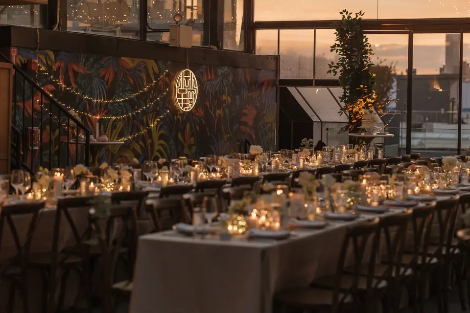 The dining room at dusk, long candlelit tables before a tropical mural and a double happiness sign.