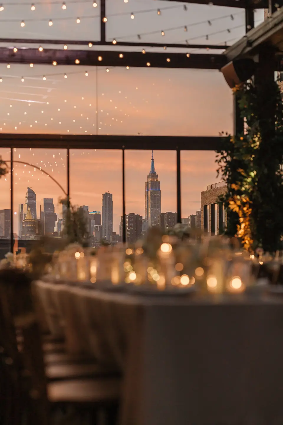 Candlelit tables beneath strings of lights, the Empire State Building framed in the window at sunset.