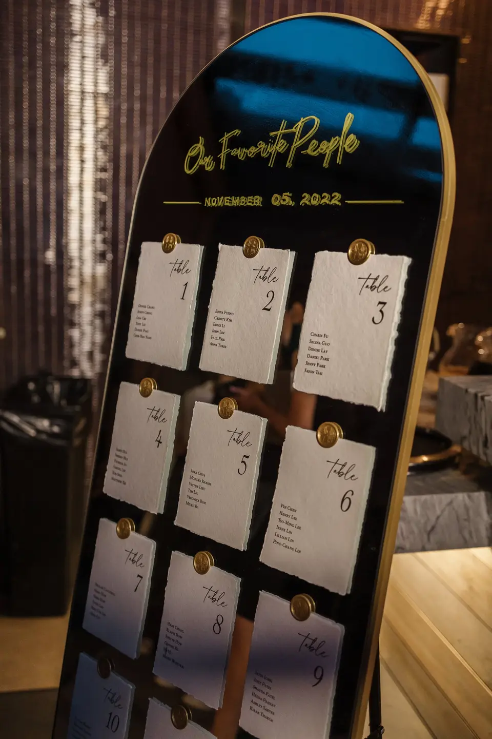 A black arched seating chart reading Our Favorite People, with table cards pinned in gold.