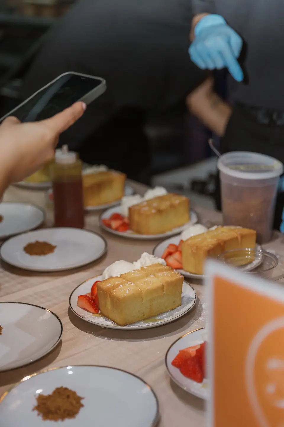 Slices of cake with strawberries and cream set out on small plates, a gloved hand serving beside them.