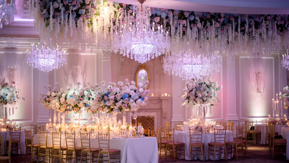 The ballroom at The Rockleigh in pink light, with crystal chandeliers, cascades of white flowers above the tables and long candlelit tables set for dinner.