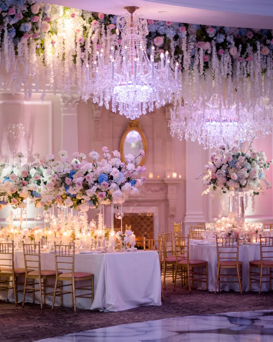 The ballroom at The Rockleigh beneath a ceiling of hanging white flowers and crystal chandeliers, tables dressed in white, blue and blush.
