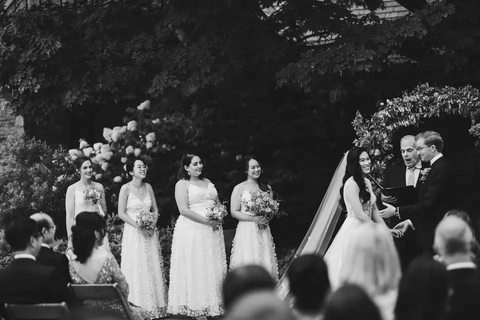 The ceremony beneath a flowered arch, the bridesmaids in a row beside the bride and groom. Black and white.