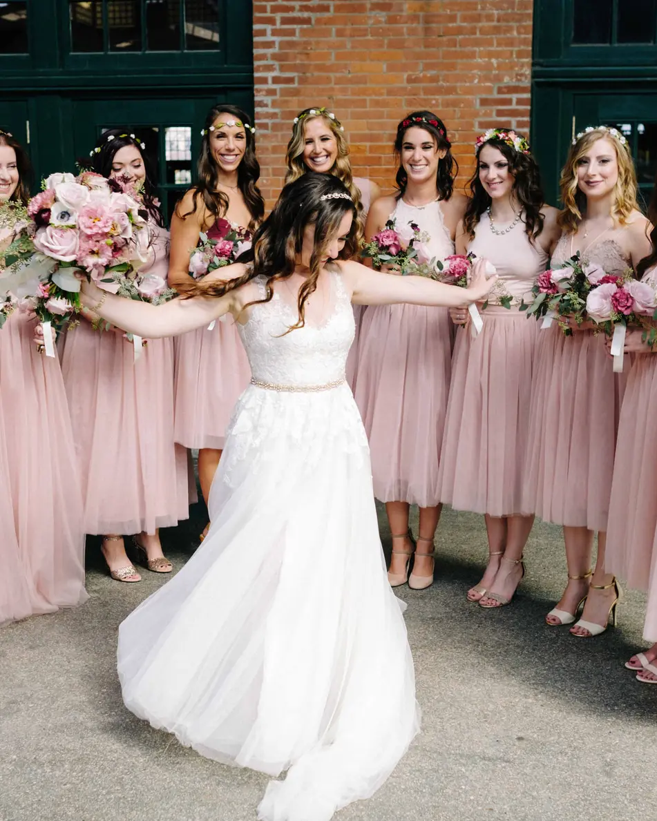 The bride spins with her arms out before her bridesmaids in blush, beneath the terminal canopy.