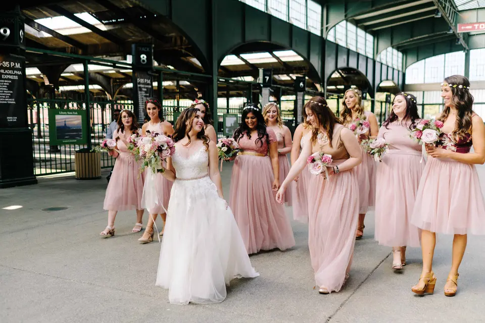 The bride walks with her bridesmaids in blush beneath the green steel canopy of the old railroad terminal.