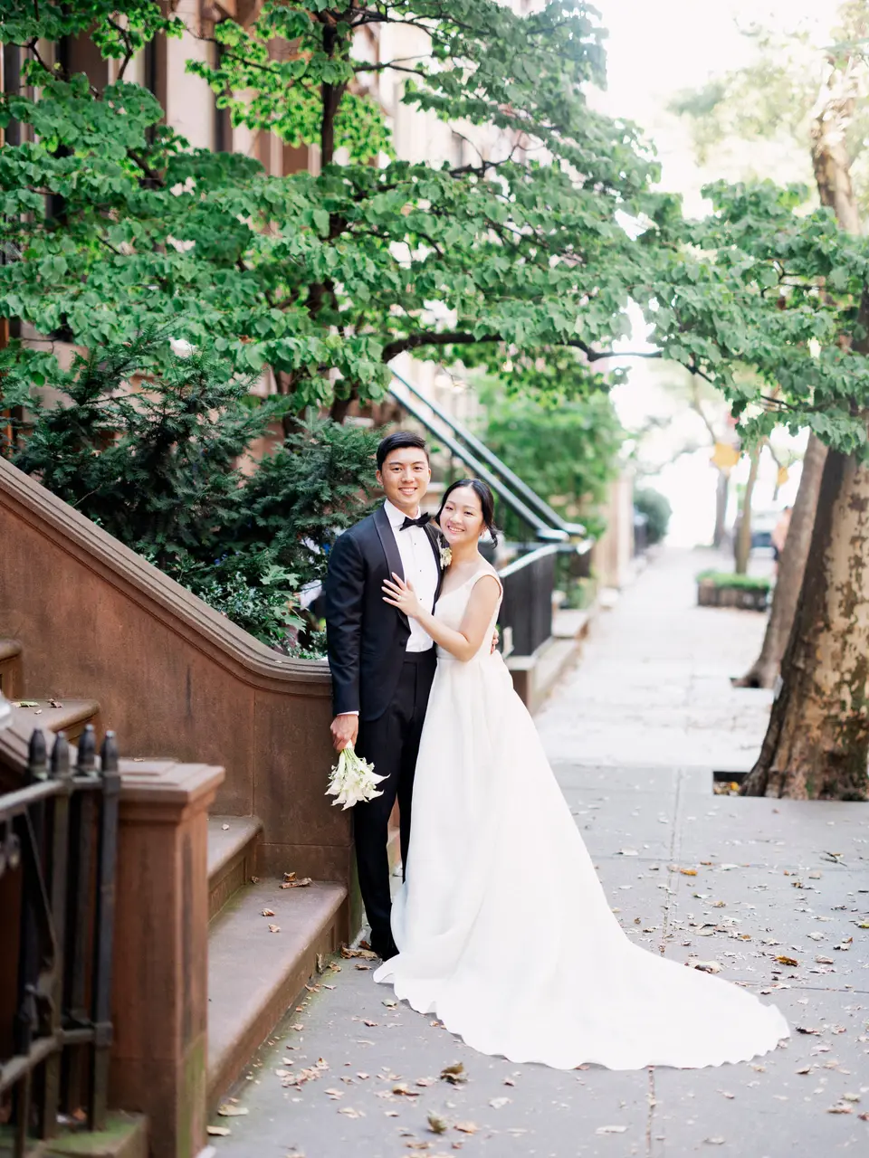 The couple stand on a leafy brownstone sidewalk in Brooklyn, the bride's long train spread across the pavement.