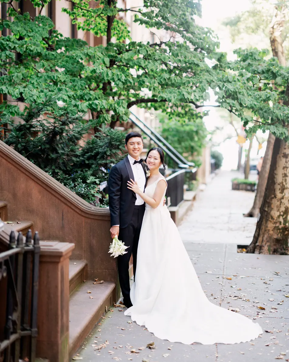 The couple stand on a leafy brownstone sidewalk in Brooklyn, the bride's long train spread across the pavement.