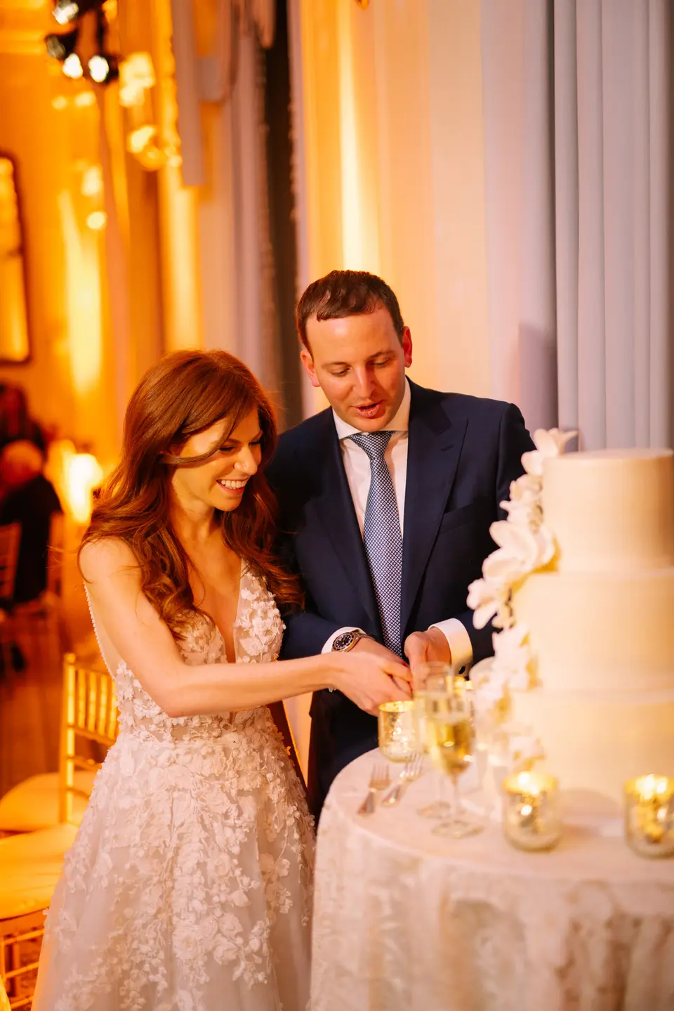 The couple cut the cake together, smiling, in warm candlelight.