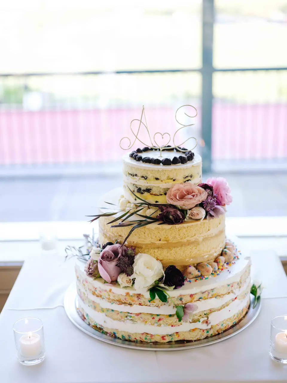 A semi-naked cake with fresh flowers on a table by the window.