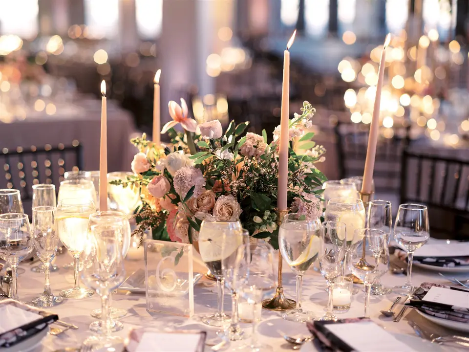 Taper candles, low flowers and crystal glasses glow on a dinner table, the room softly out of focus behind.