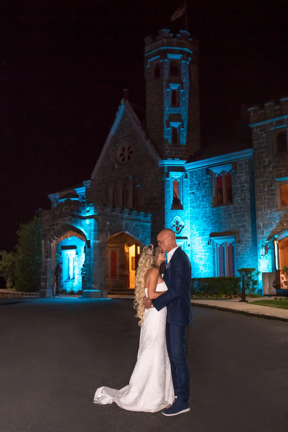 The couple kiss in the dark beneath the castle tower, its walls lit in blue.