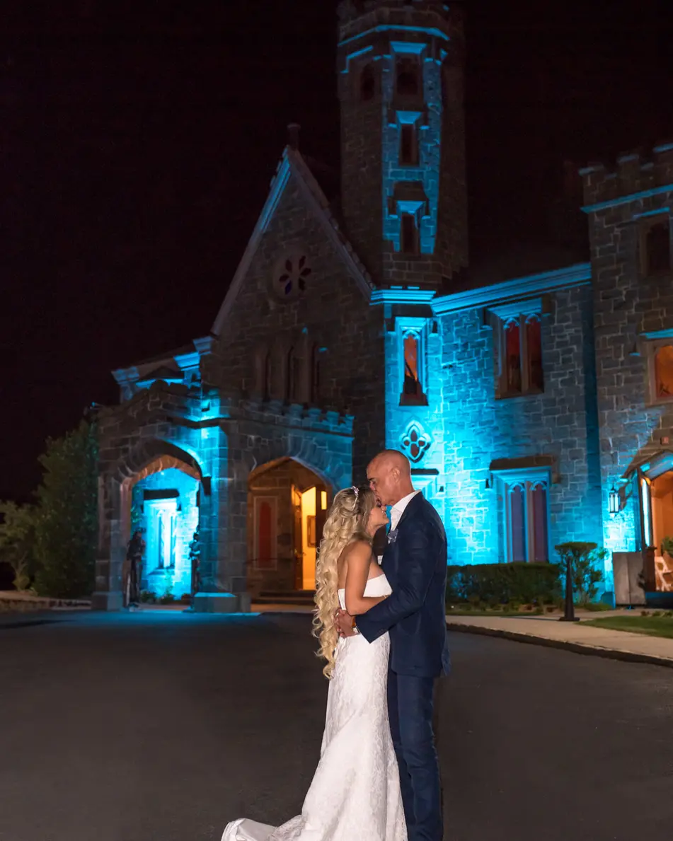 The couple kiss in the dark beneath the castle tower, its walls lit in blue.