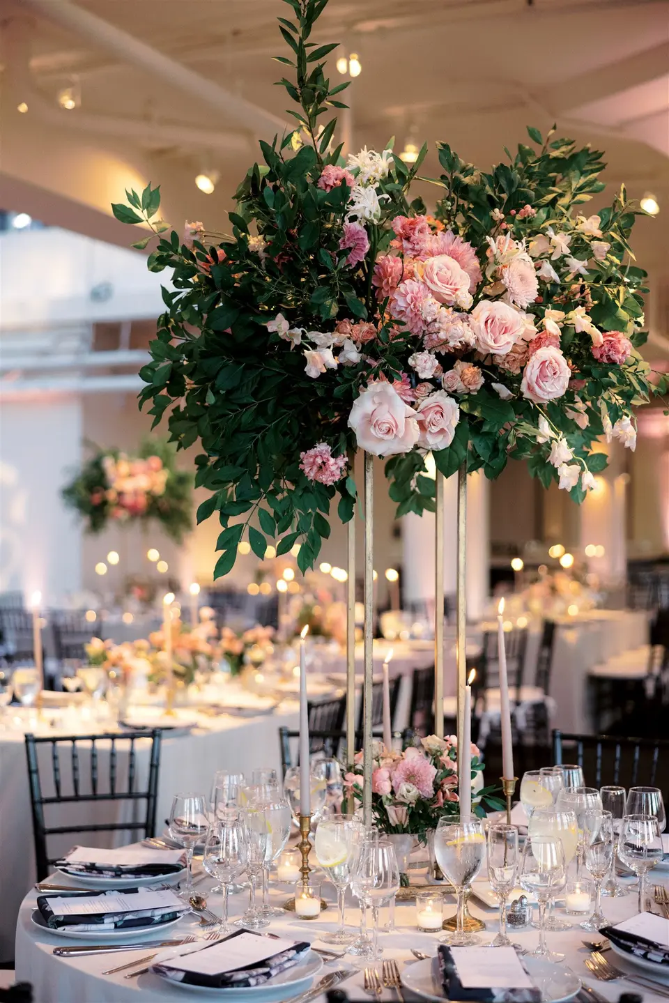 Garden roses in blush and pink spill from a tall gold stand above crystal glassware.