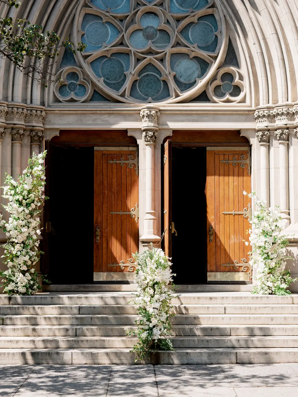 The carved wooden doors of Queen of All Saints church in Brooklyn, the stone steps and railings trailing white flowers.