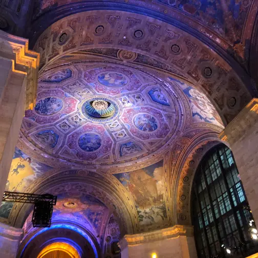 The painted and gilded dome of the Great Hall of the Cunard Building at 25 Broadway, lit in violet and gold for an evening event.