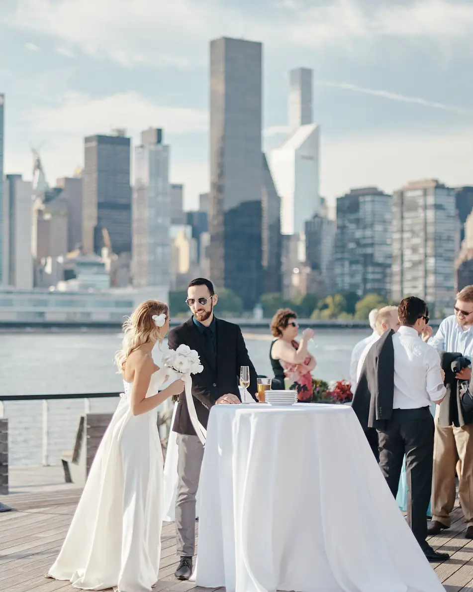Guests mingle at cocktail tables on the deck, the United Nations and Midtown towers across the river.