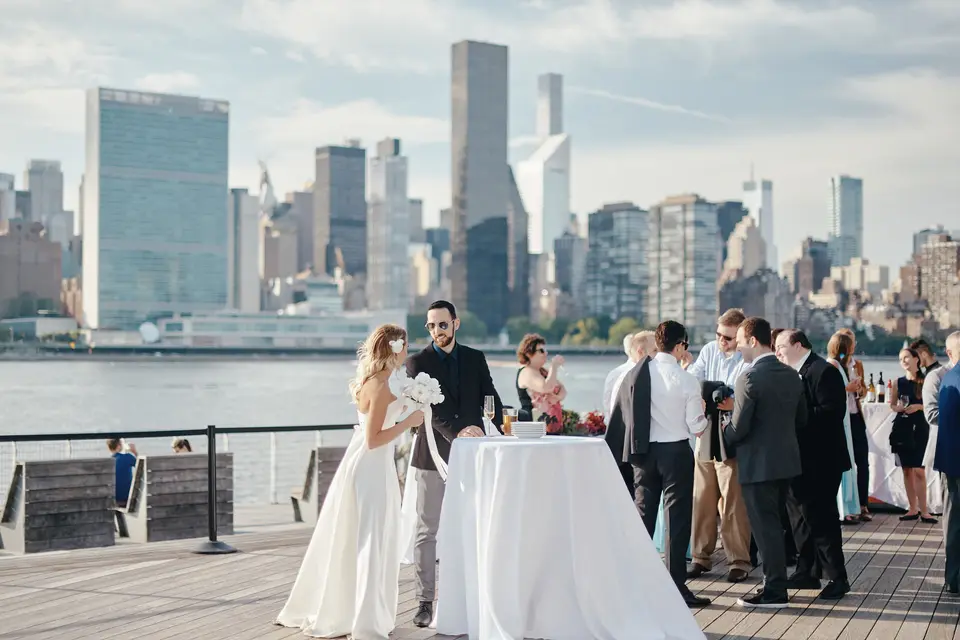 Guests mingle at cocktail tables on the deck, the United Nations and Midtown towers across the river.