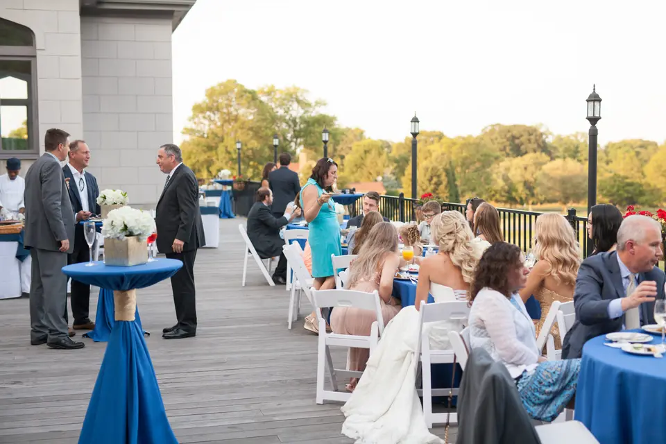 Guests at cocktail tables in blue linen on a wooden terrace overlooking the grounds.