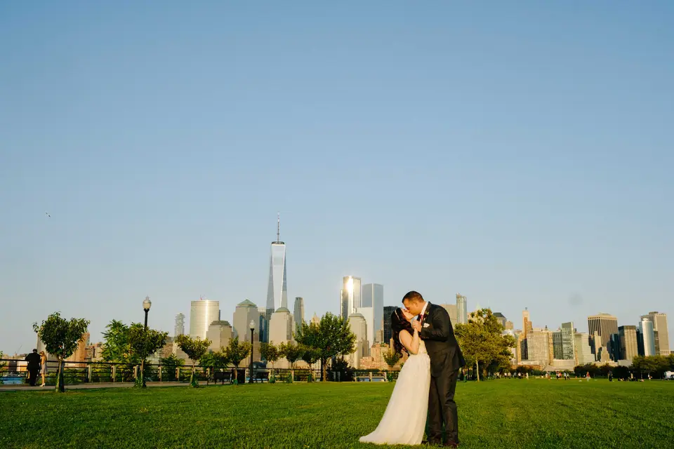 The couple kiss on the lawn at Liberty State Park, the towers of Lower Manhattan and One World Trade Center across the water.