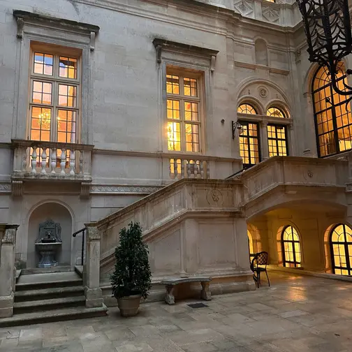 The stone courtyard of the Burden Kahn Mansion at dusk, its windows glowing above balustraded steps.