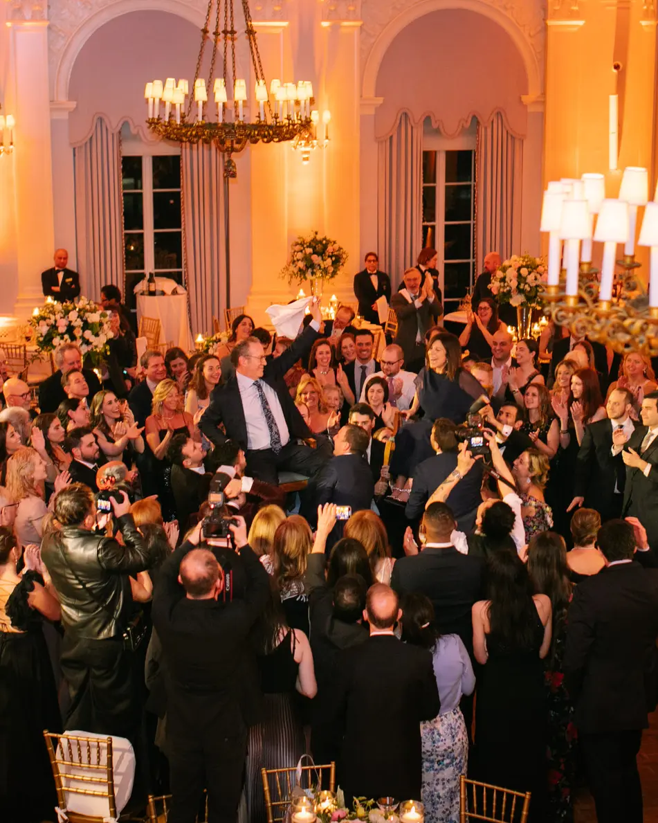 Seen from above, guests fill the dance floor of the ballroom beneath chandeliers and warm light.