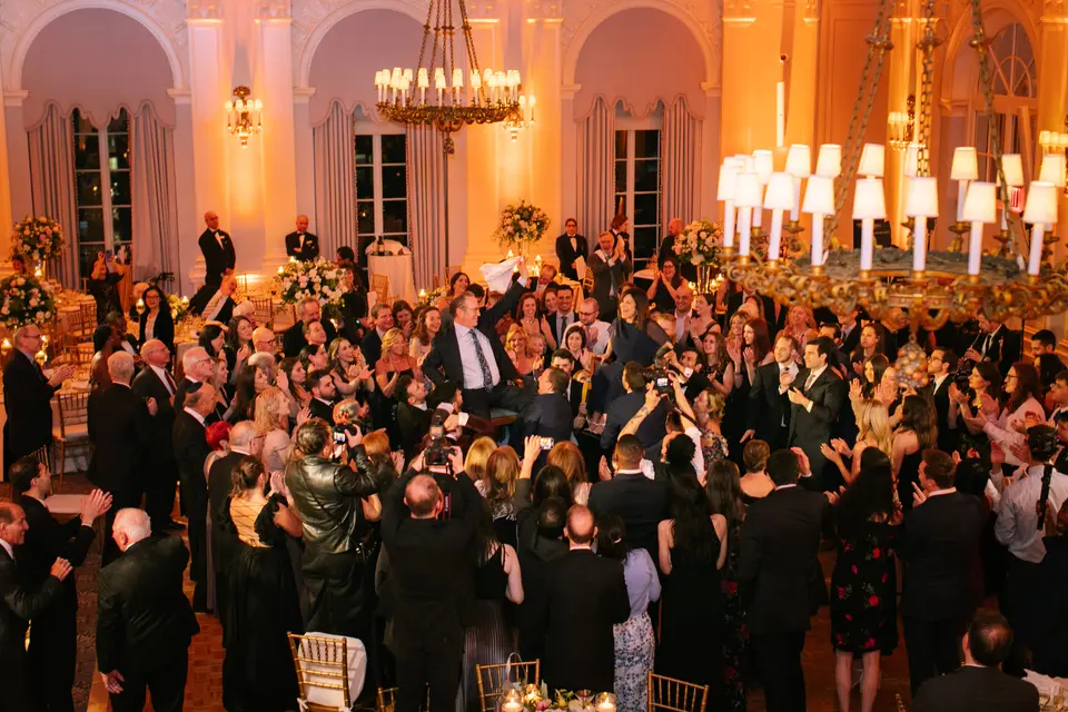 Seen from above, guests fill the dance floor of the ballroom beneath chandeliers and warm light.