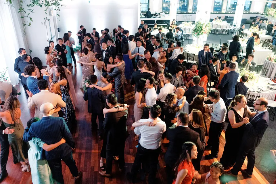 Guests fill the dance floor at Tribeca Rooftop, couples swaying in close dance seen from above, round dinner tables and tall windows beyond.