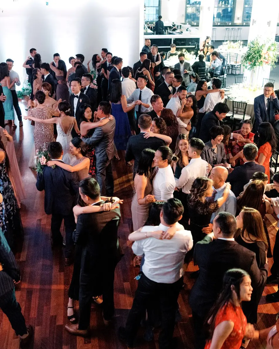 Seen from above, guests fill the dance floor, couples holding one another beneath hanging greenery.