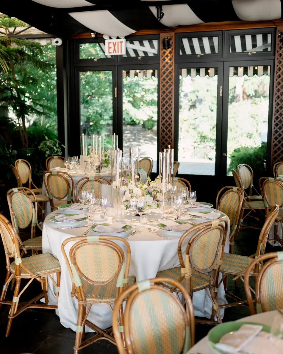A round table dressed in white with rattan chairs, candles and white flowers, beneath the striped ceiling of the restaurant.