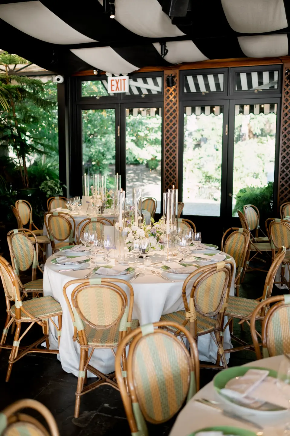 A round table dressed in white with rattan chairs, candles and white flowers, beneath the striped ceiling of the restaurant.