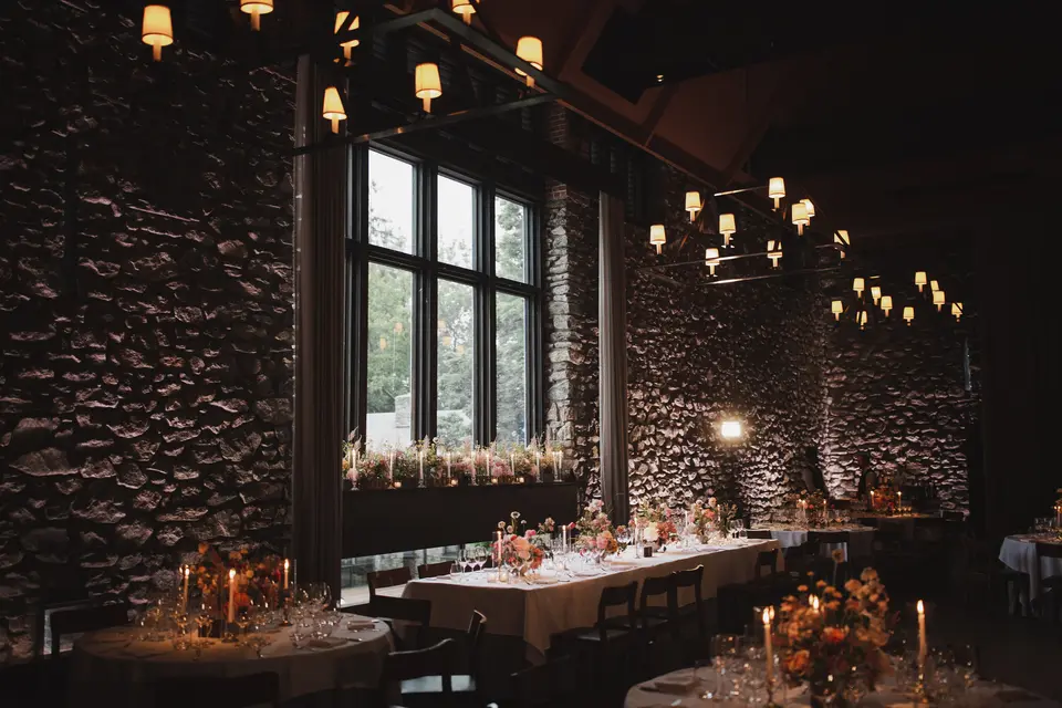 The dining room with stone walls, tall windows and iron chandeliers, long tables lit by candles and flowers.
