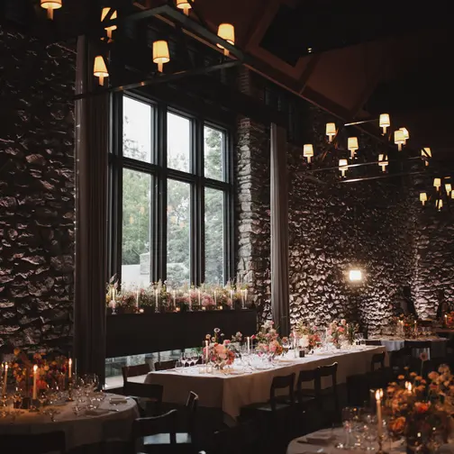 The dining room at Blue Hill at Stone Barns, with stone walls, tall windows and iron chandeliers, long tables lit by candles and flowers.