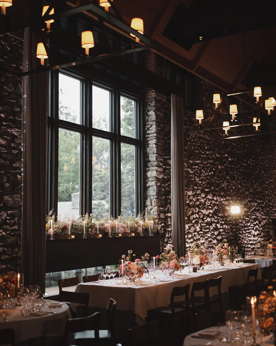 The stone-walled dining room at dusk, long candlelit tables with flowers beneath iron chandeliers.