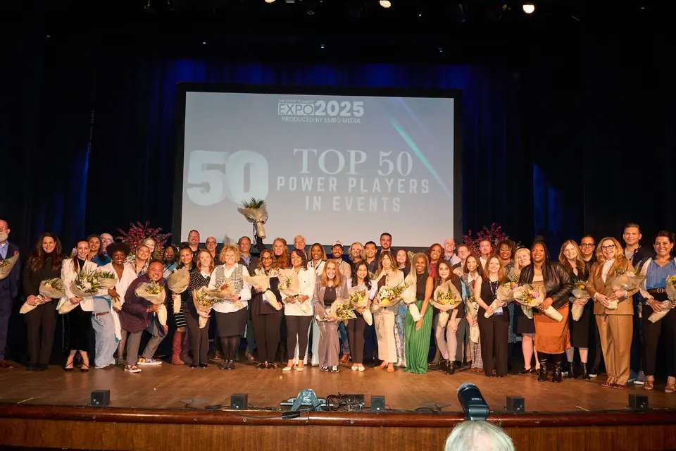 The Top 50 Power Players in Events stand together on stage holding bouquets, the title projected on the screen behind them.