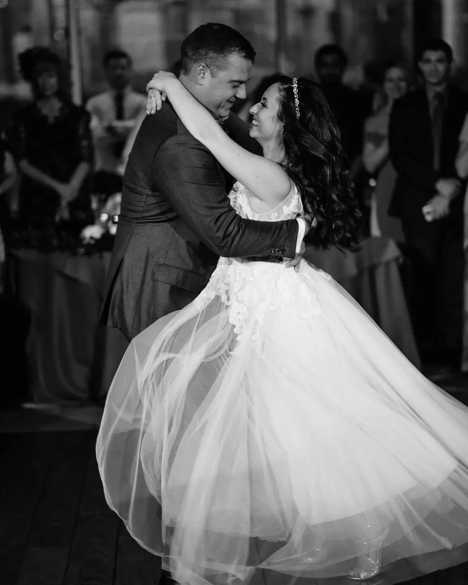 The couple turn in their first dance, the bride's skirt swinging out. Black and white.