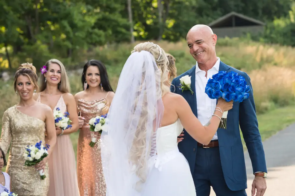 The groom, in a blue suit, beams as he sees the bride for the first time, her bridesmaids in gold and blush beside them.