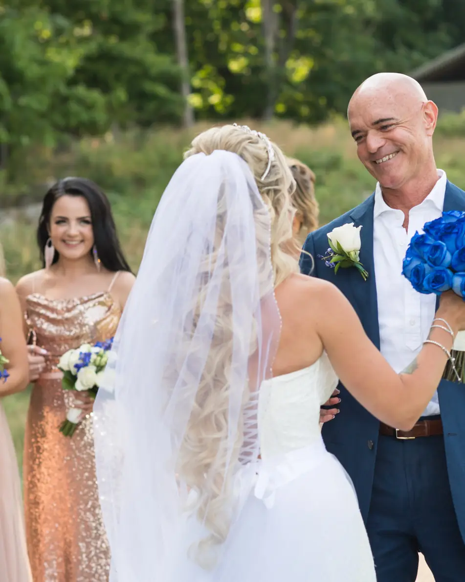 The groom, in a blue suit, beams as he sees the bride for the first time, her bridesmaids in gold and blush beside them.