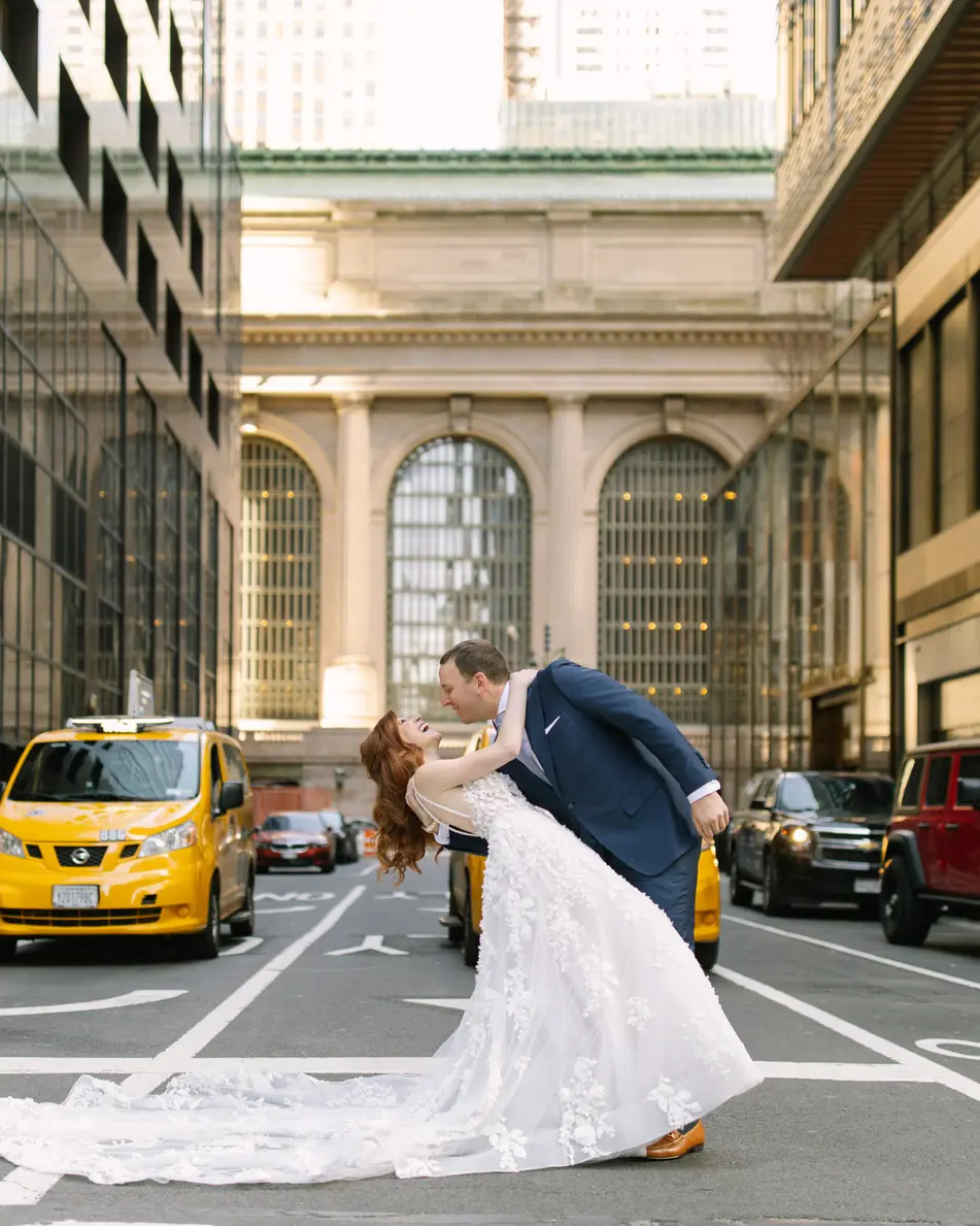 In the middle of Vanderbilt Avenue, the groom dips the bride for a kiss, Grand Central's arched windows behind them and a yellow taxi waiting.