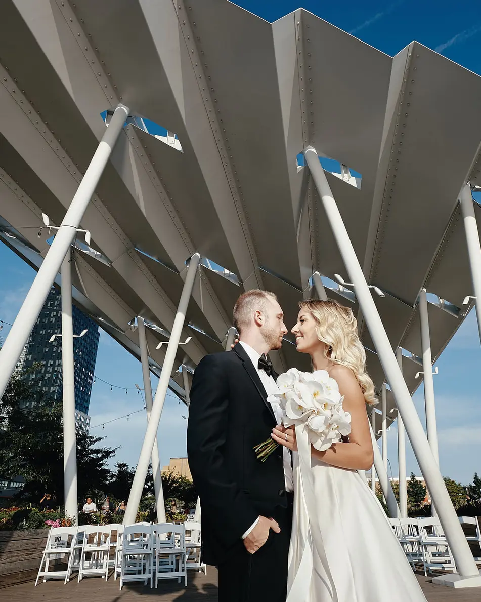 The couple kiss beneath the white canopy against a deep blue sky.