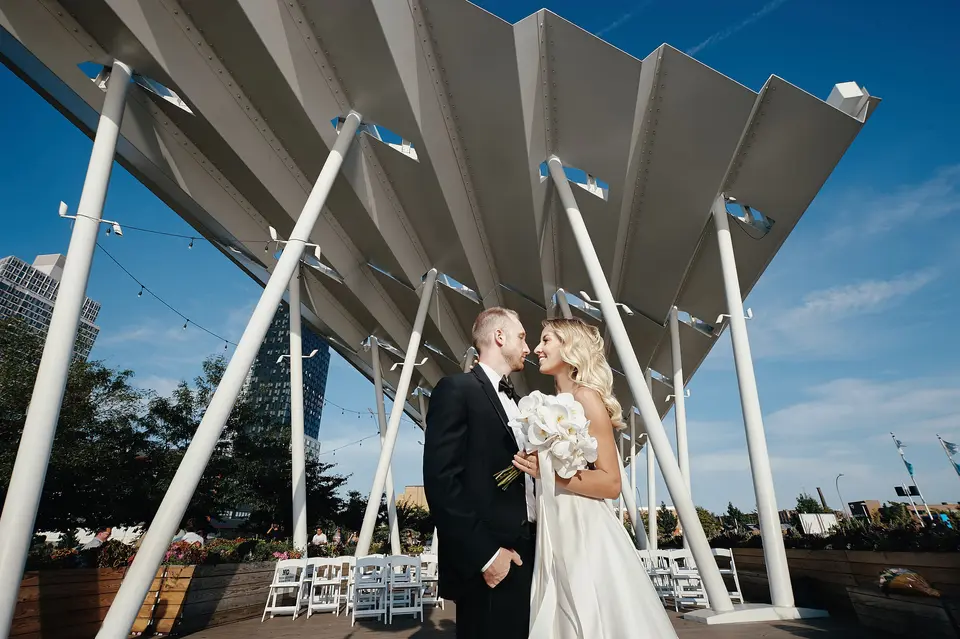 The couple kiss beneath the white canopy against a deep blue sky.