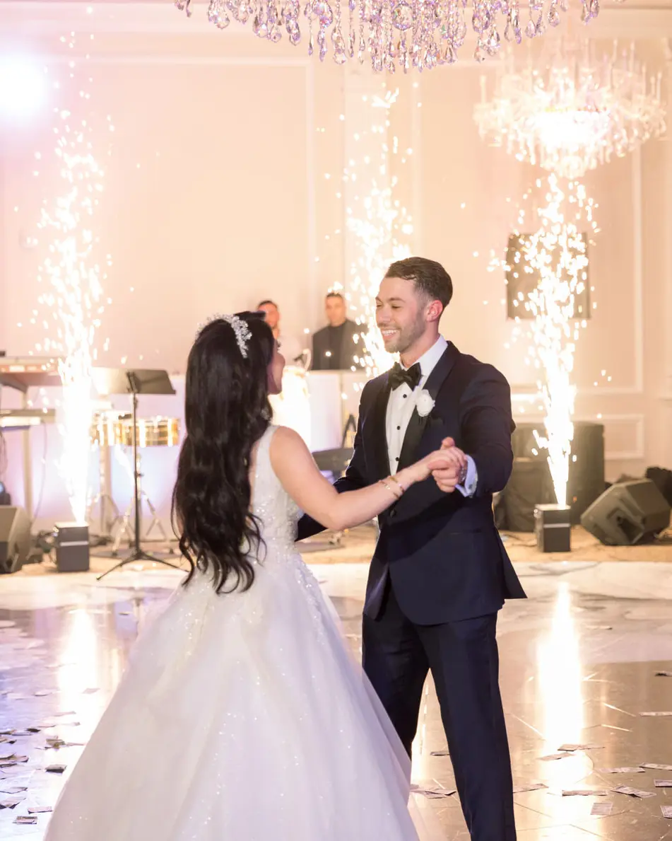 The couple dance as tall fountains of sparks rise behind them in the ballroom.