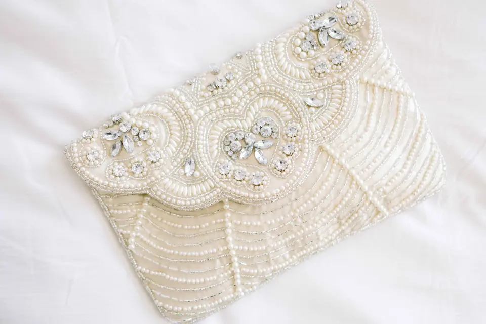 A beaded ivory clutch with a scalloped flap, laid on white linen.