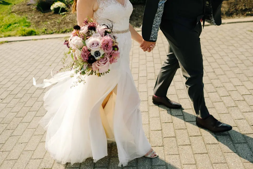 The bride and groom walk hand in hand across the pavers, her gown catching the light.