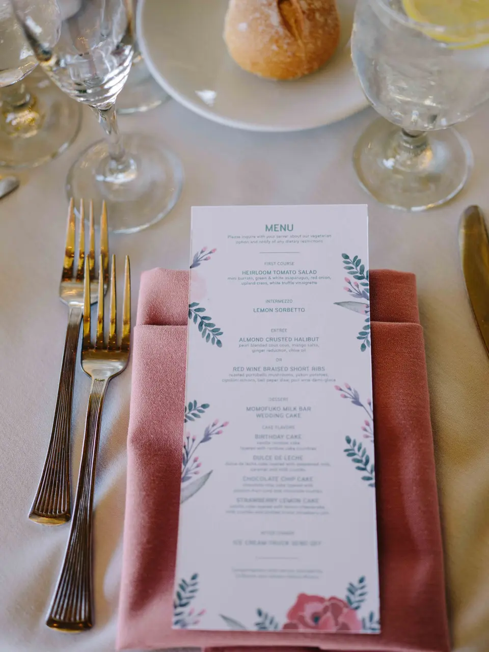 A menu card with watercolor leaves on a dusty pink napkin, gold cutlery on either side.