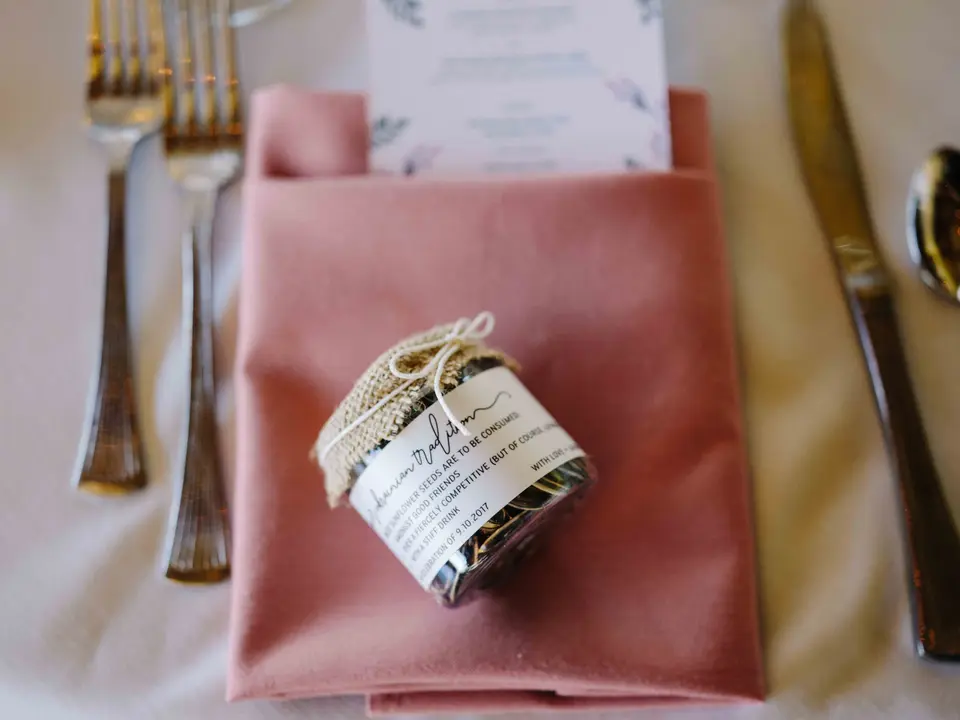 A small jar favor wrapped in burlap and twine, set on a dusty pink napkin.