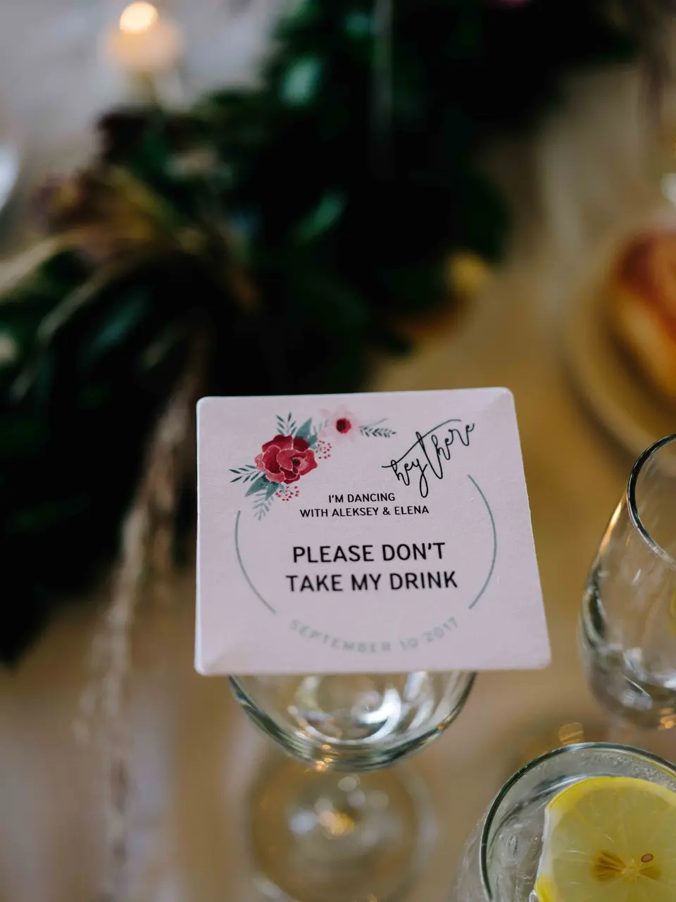A coaster on a glass reading Please don't take my drink, painted with a red rose.