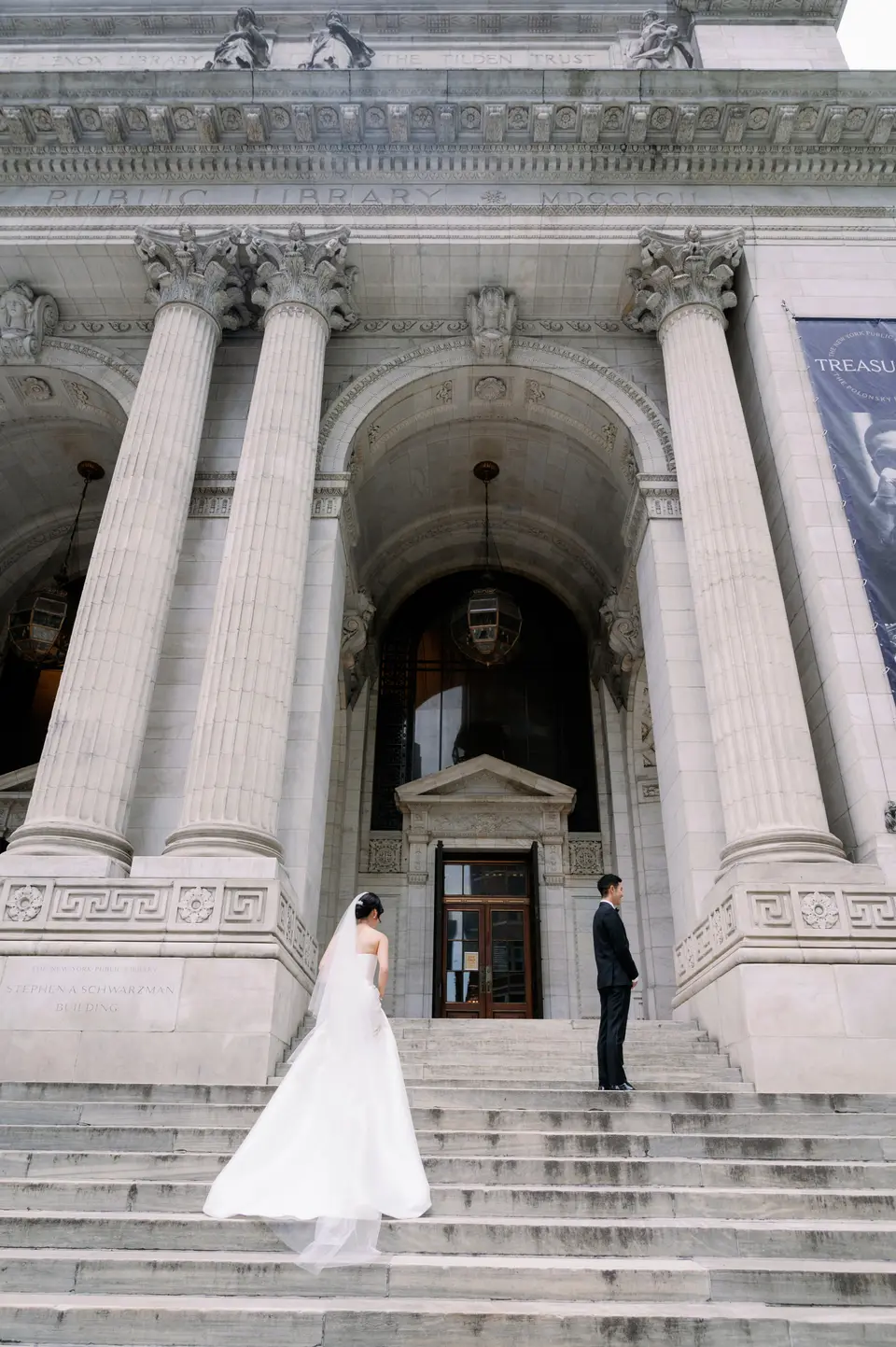 The bride and groom stand on the wide stone steps of the New York Public Library on Fifth Avenue, between its great columns.