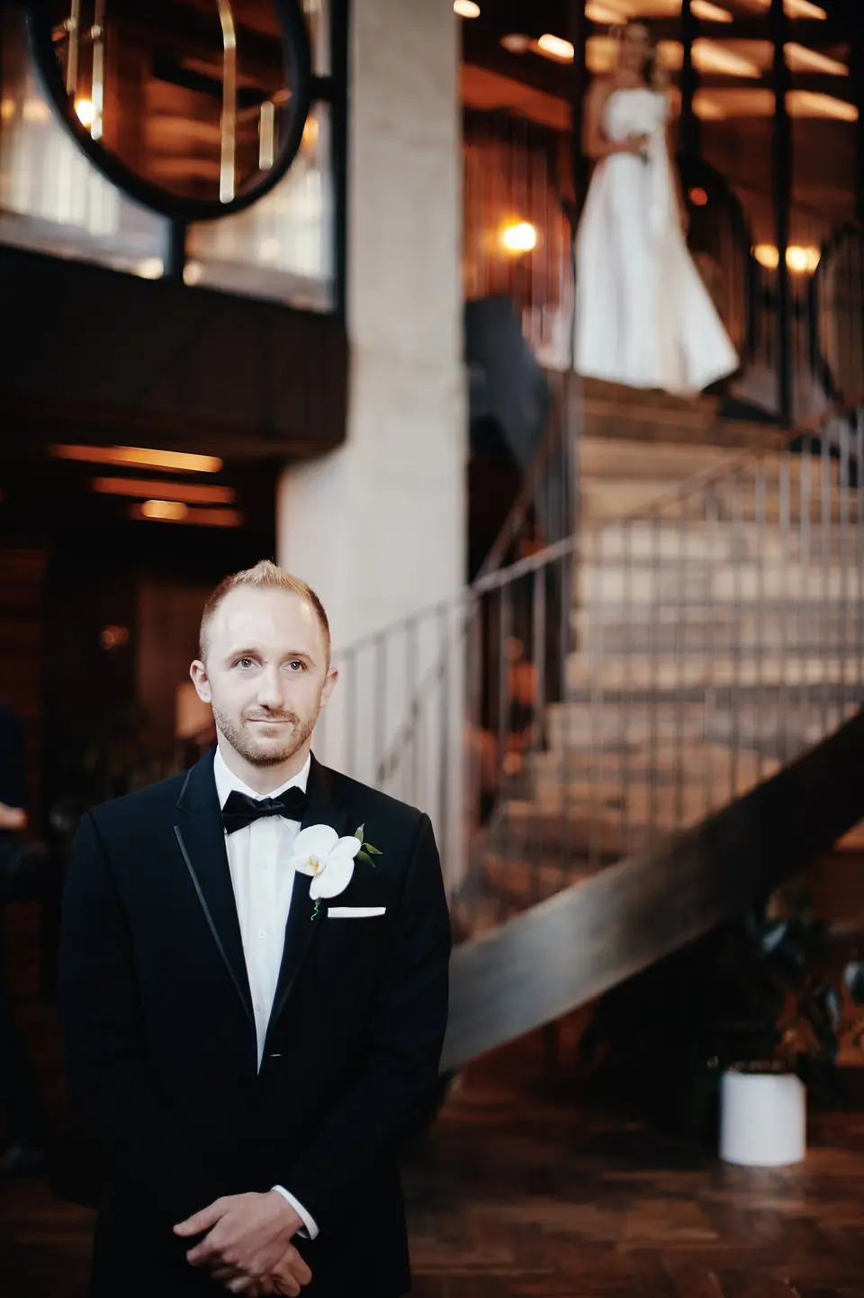 The groom waits at the foot of a spiral staircase as the bride appears at the top.