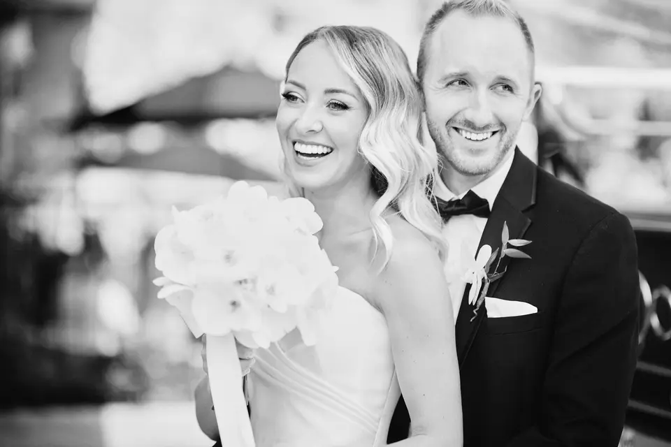 The bride and groom laugh together, her bouquet of white orchids between them. Black and white.